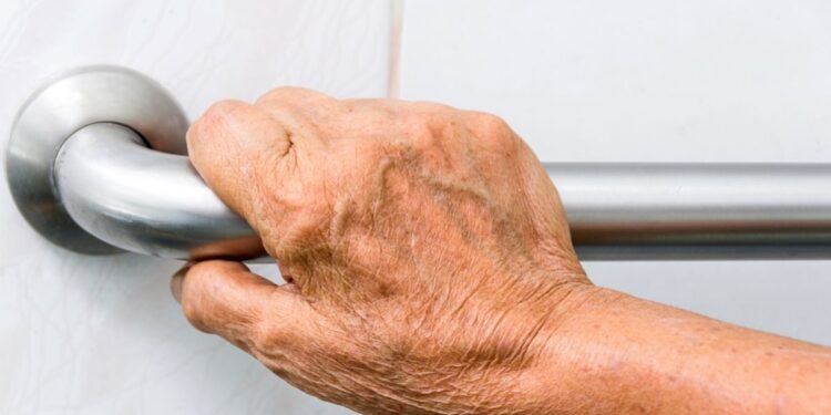 A senior man holding the shower standing handle for support