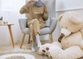 A women sitting on the chair sipping tea with a teddy bear placed beside her on the ground